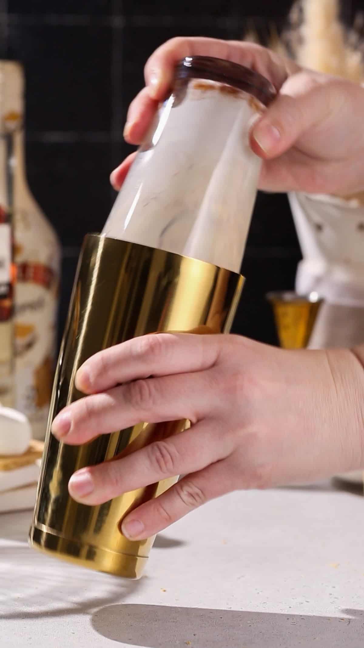 Hand shaking up a cocktail in a gold and glass cocktail shaker.