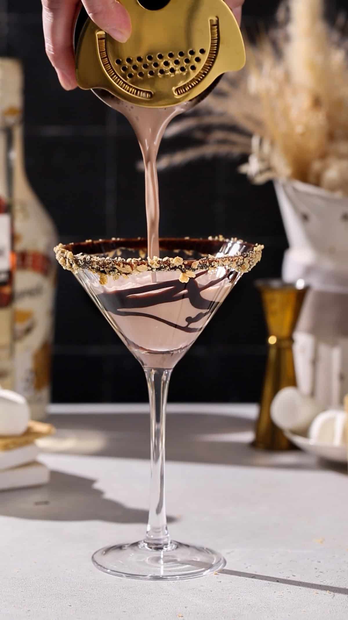 Hand straining a smores cocktail into a martini glass.