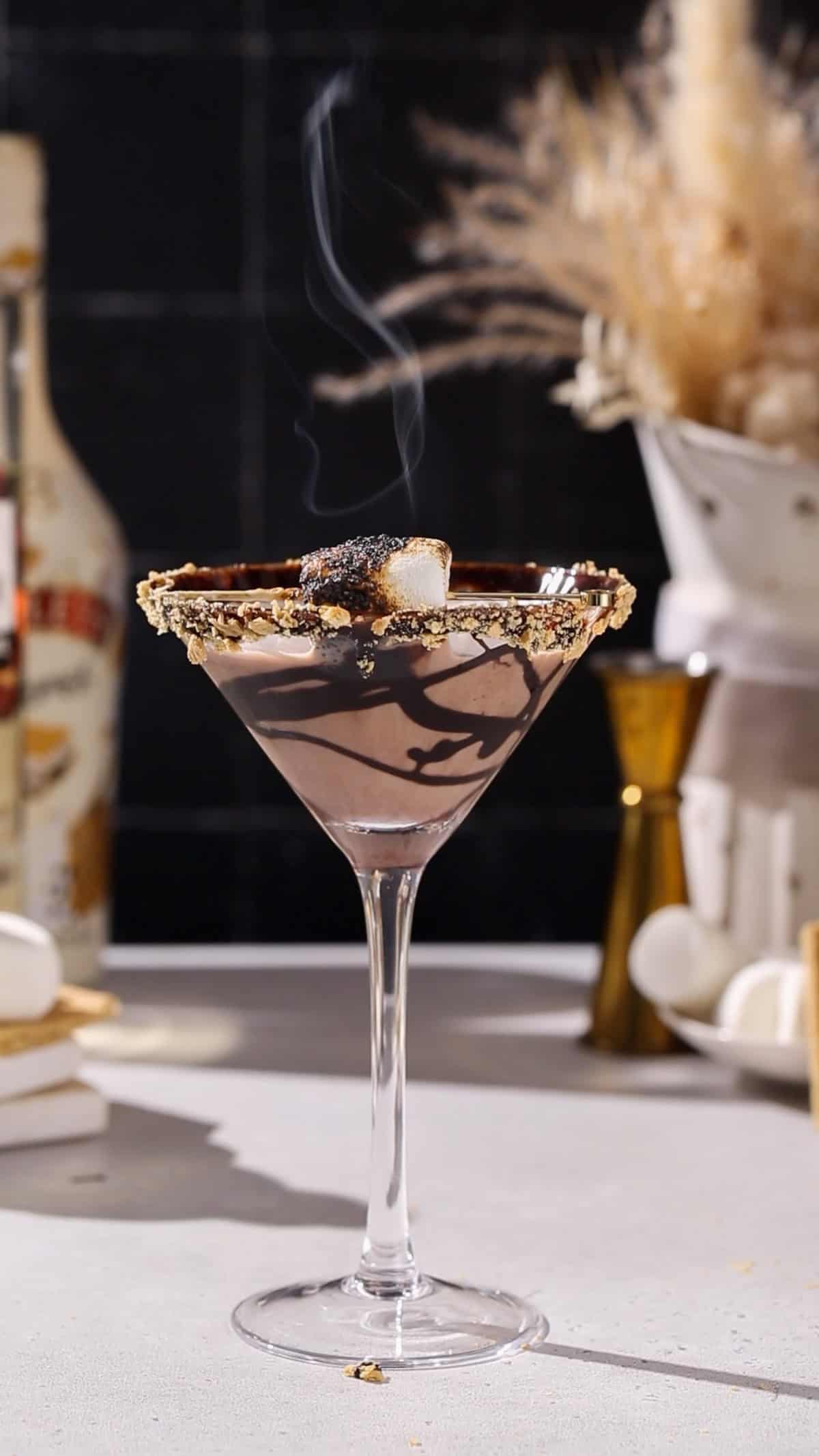 Smores martini with smoke coming off of a toasted marshmallow on top of the drink.