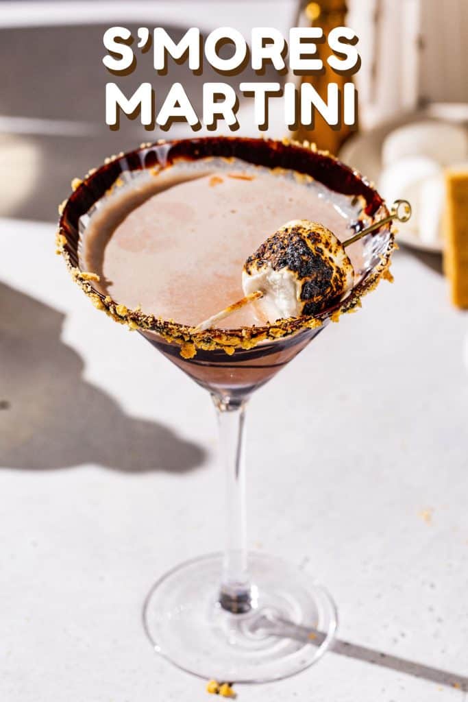 Slightly overhead view of a smores martini with a toasted marshmallow garnish. Text at the top of the image says “S’Mores Martini”.