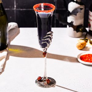 Black Mimosa cocktail on a countertop with red sugar in a small dish in the background as well as a bottle of Prosecco.