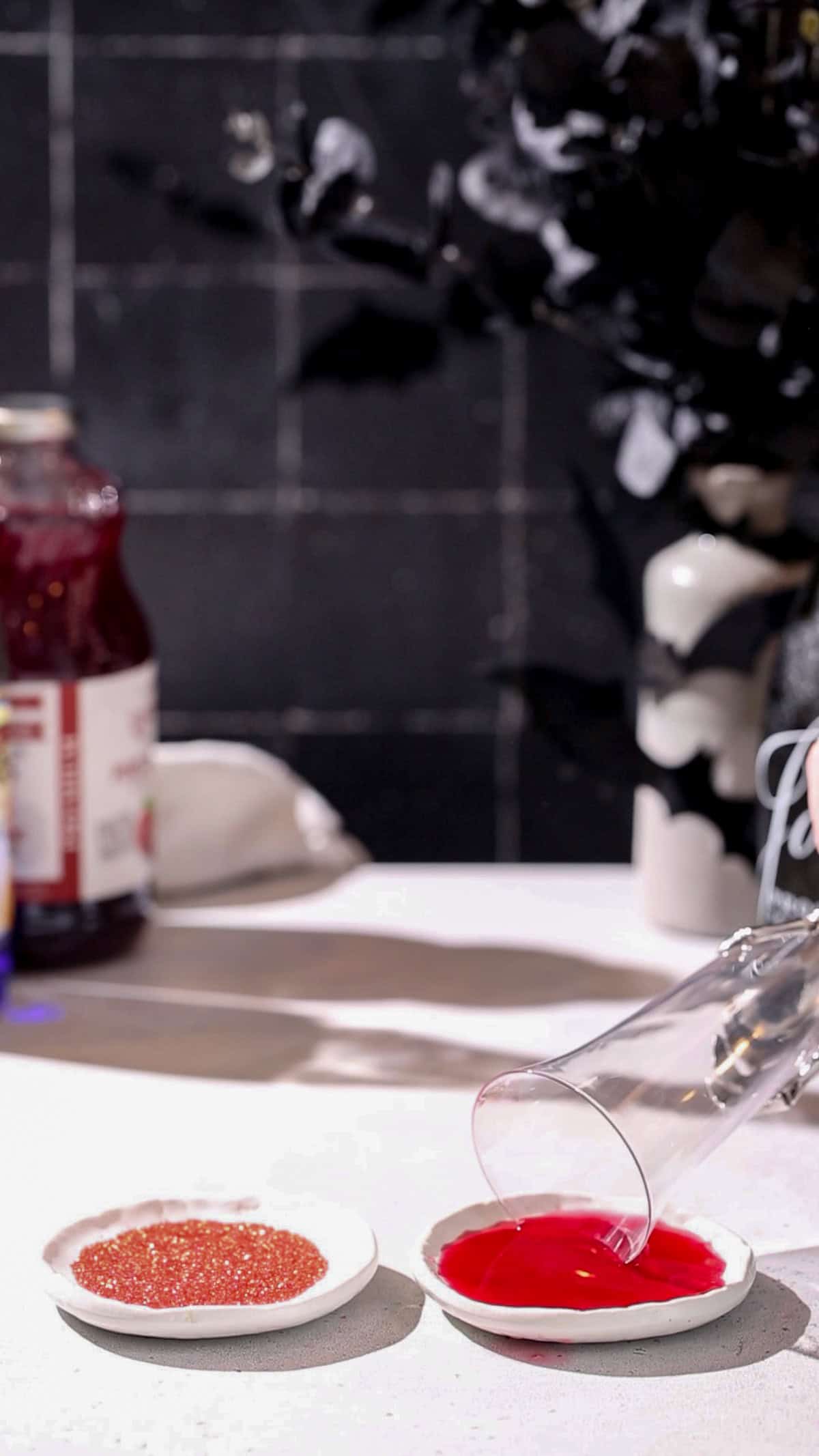 Hand dipping the rim of a cocktail glass into a dish of cranberry juice.