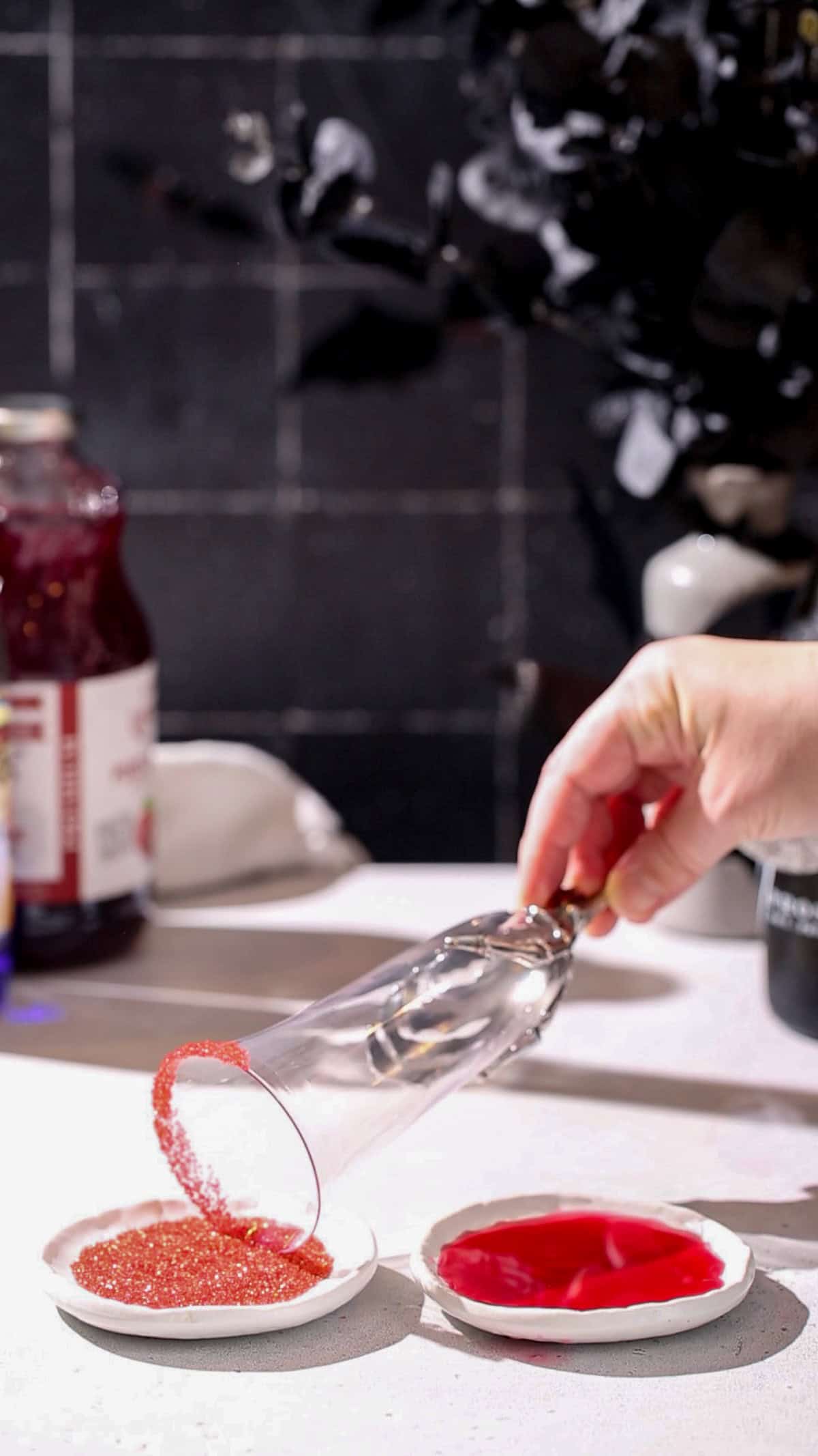 Hand dipping the rim of a cocktail glass into a dish of red sugar.