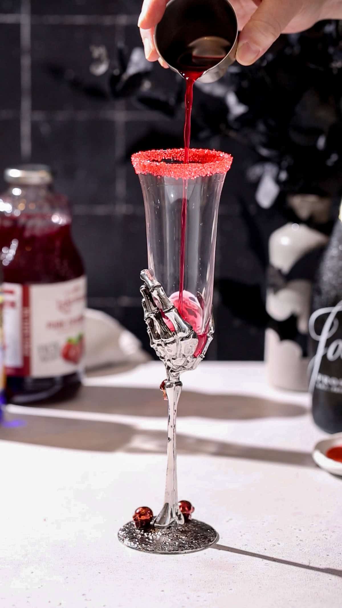 Hand pouring cranberry juice into a champagne flute.