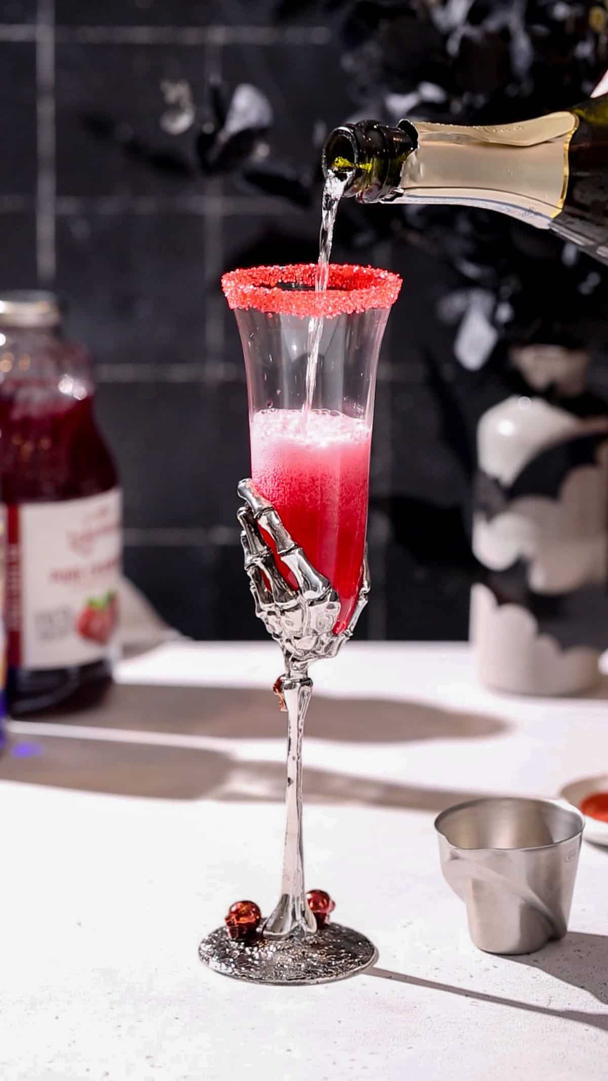 Hand pouring prosecco into a champagne flute that has cranberry juice in it, so the liquid looks red in color.