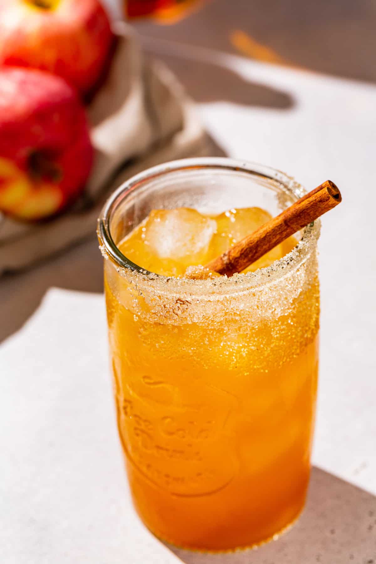 Fireball Apple Cider cocktail with a cinnamon stick garnish and an apple in the background.