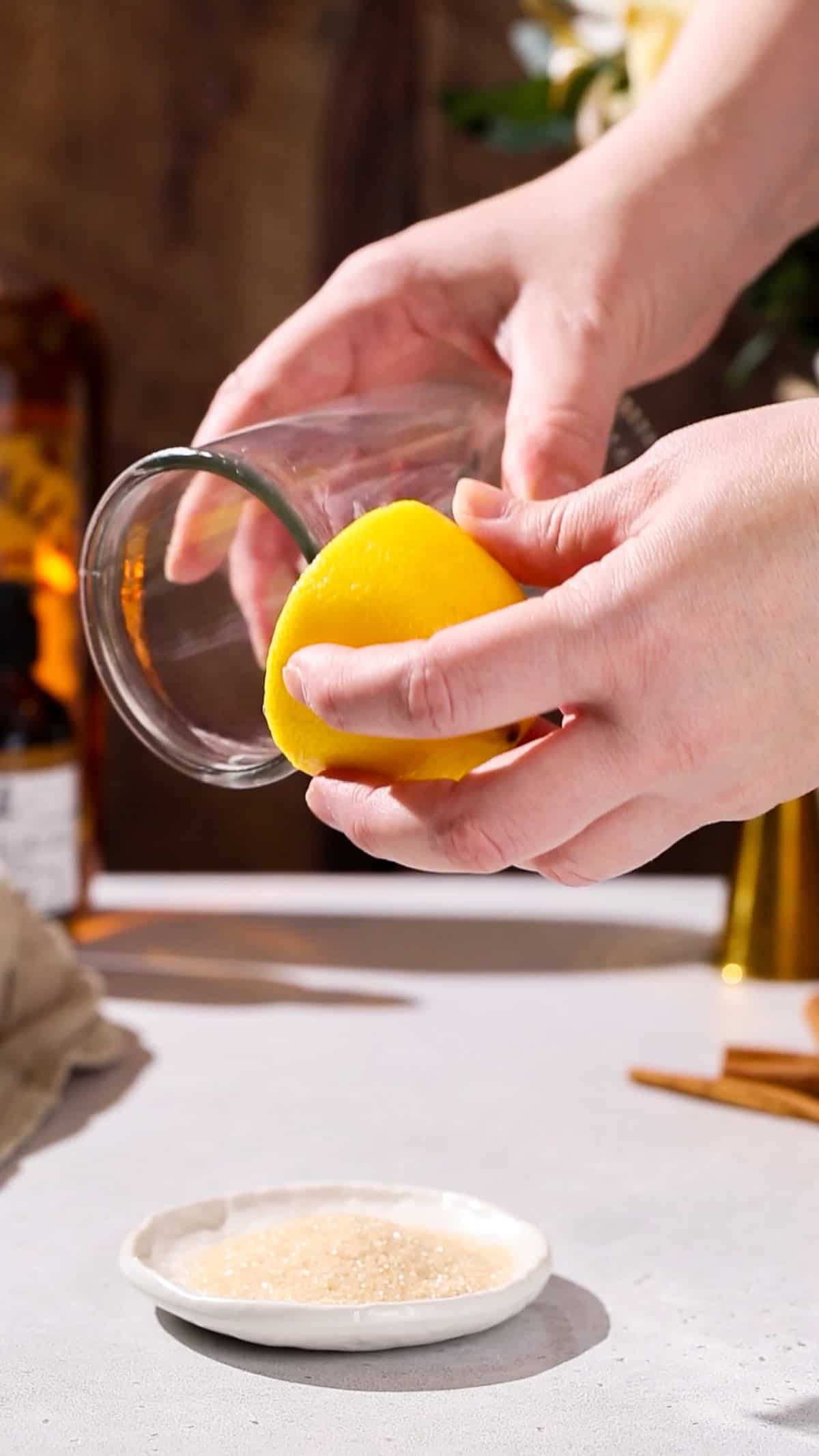 Hand using a cut lemon to wet the rim of a cocktail glass.