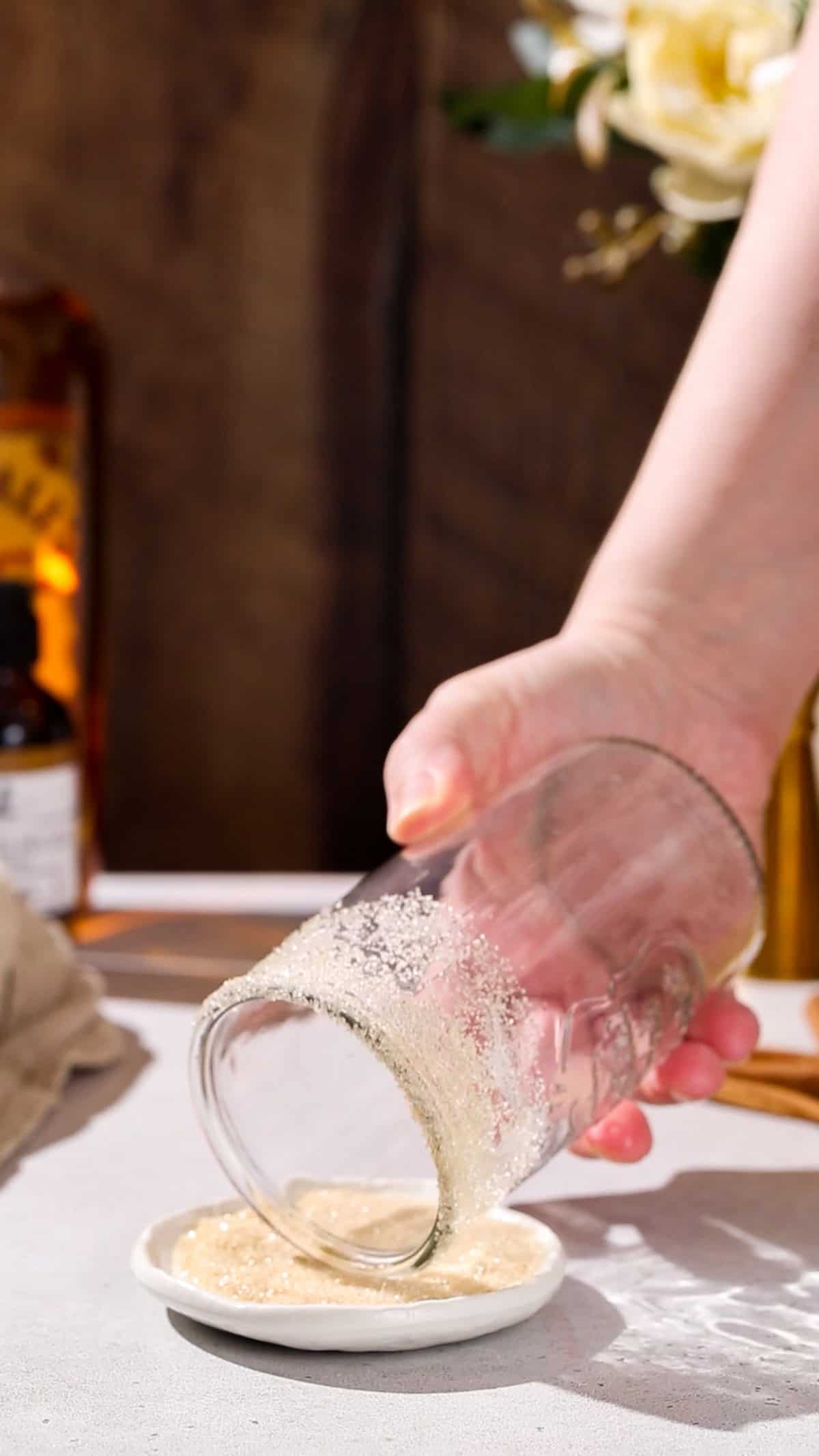 Hand dipping the rim of a glass in cinnamon sugar.