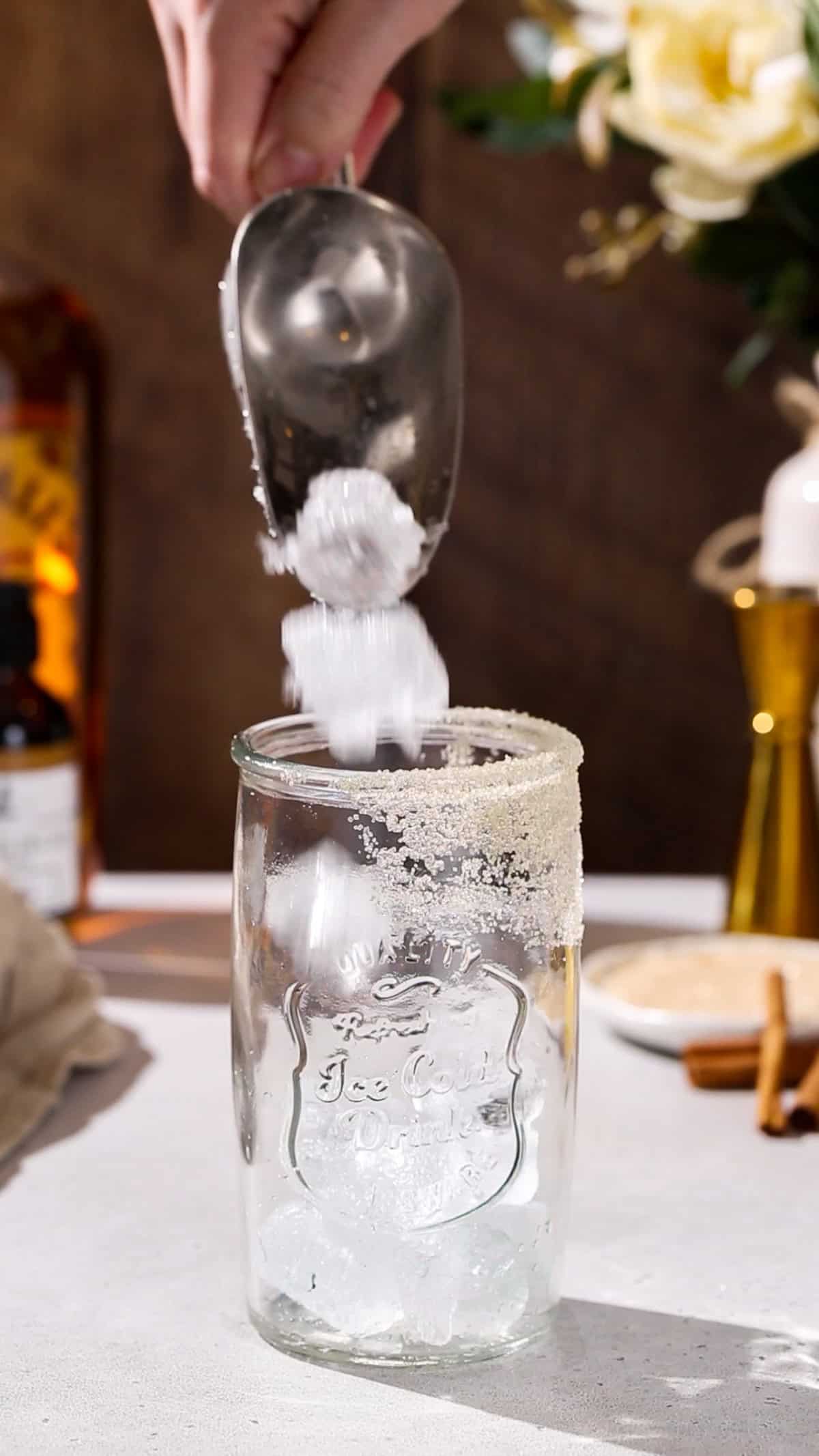 Hand using an ice scoop to fill a glass with ice.