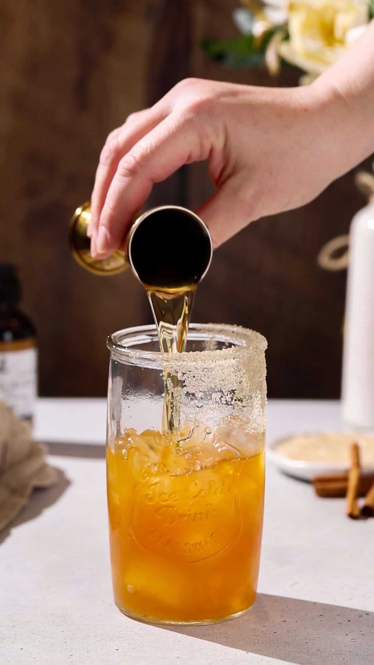 Hand adding fireball whiskey to a cocktail glass.