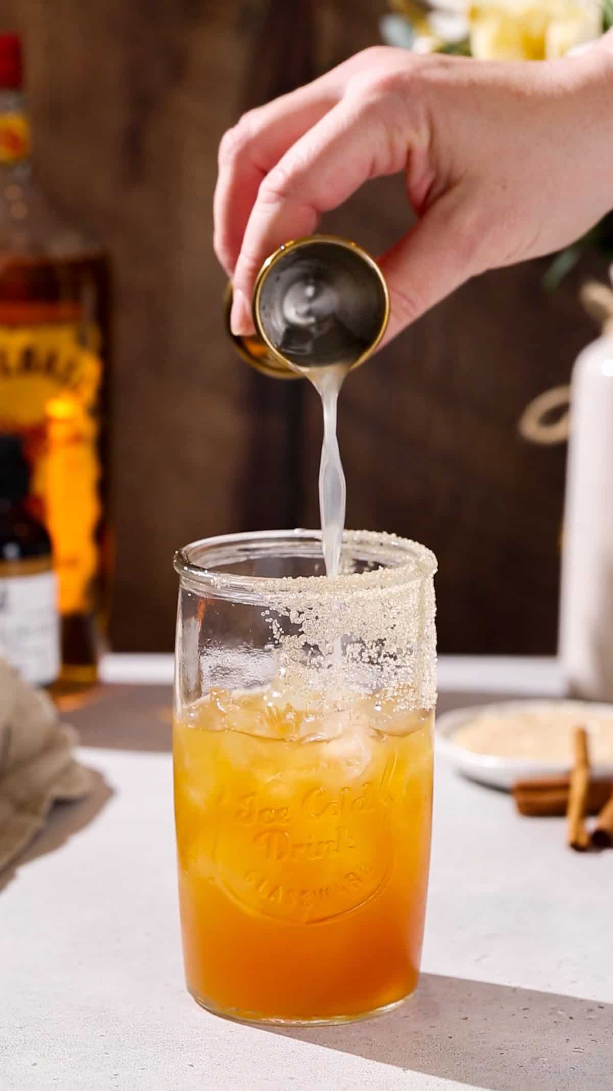 Hand adding lemon juice to a cocktail glass.