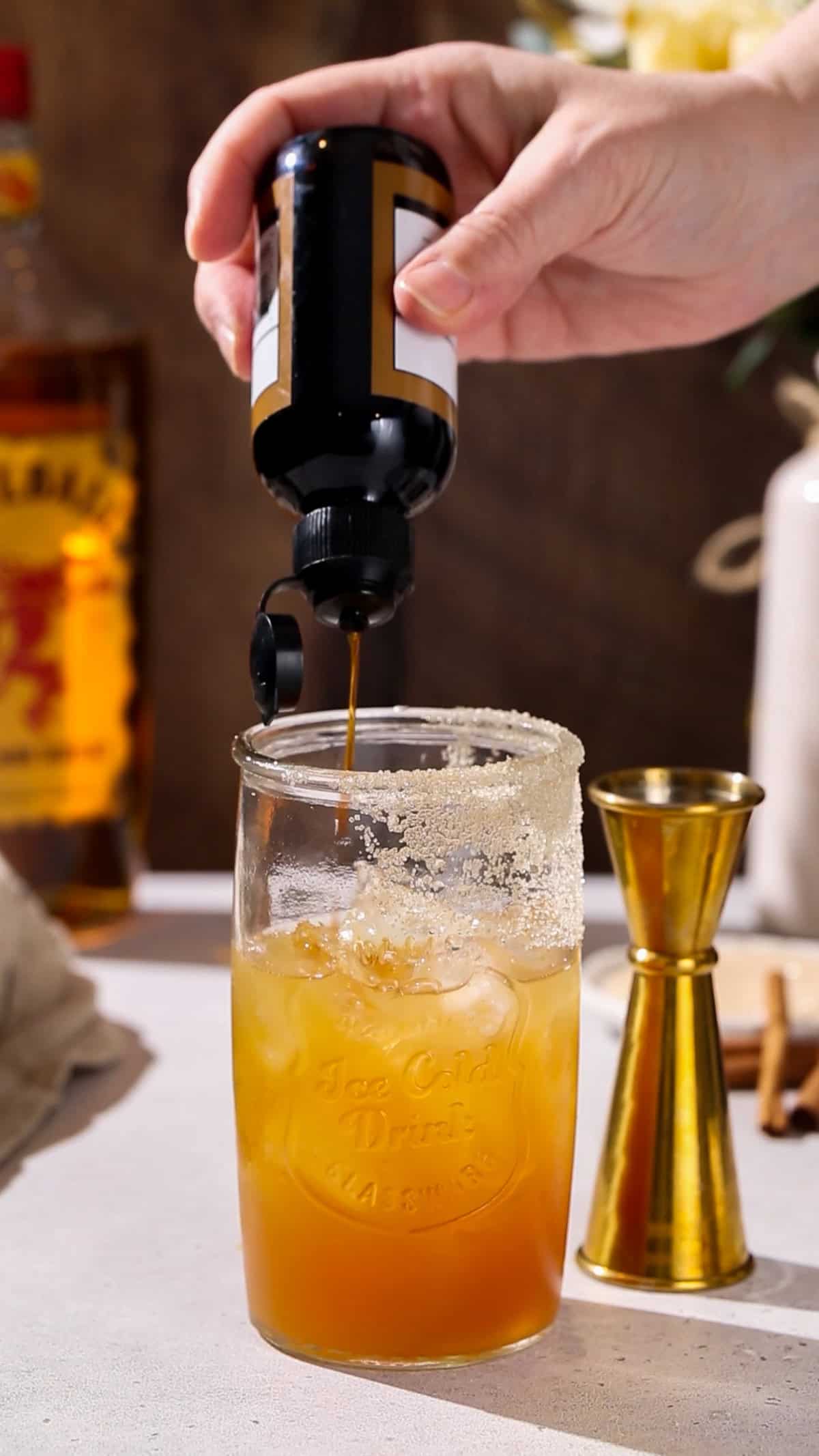 Hand adding toasted pecan bitters to a cocktail glass.