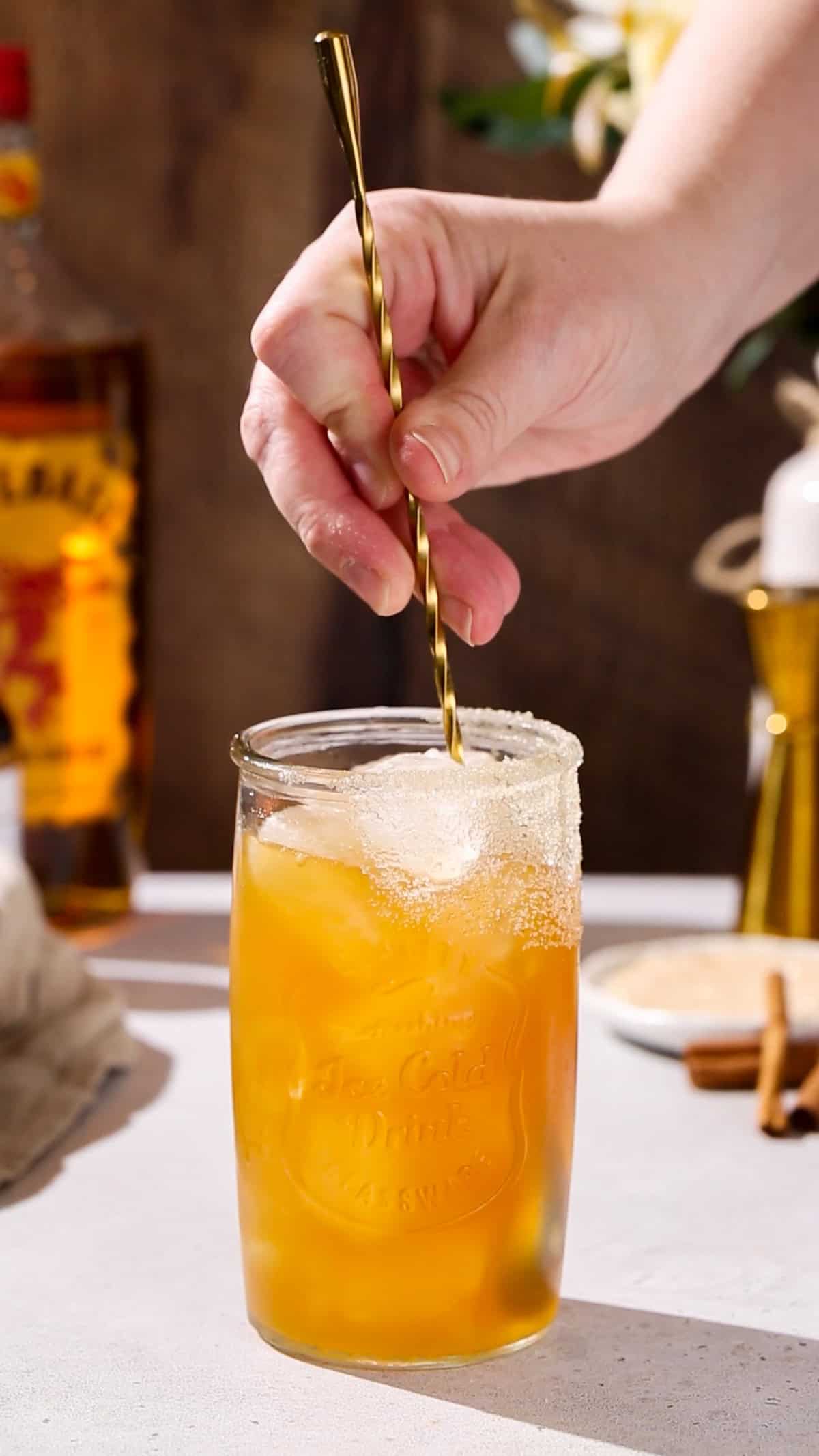 Hand using a long bar spoon to stir a cocktail.