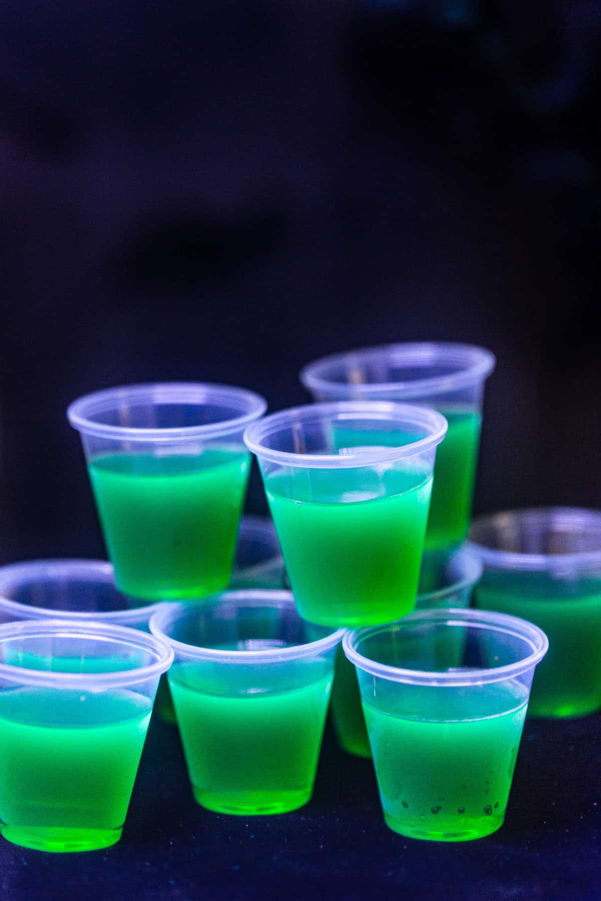 Glowing green jello shots shown under a blacklight. The glow in the dark jello shots shine brightly under the ultraviolet light.