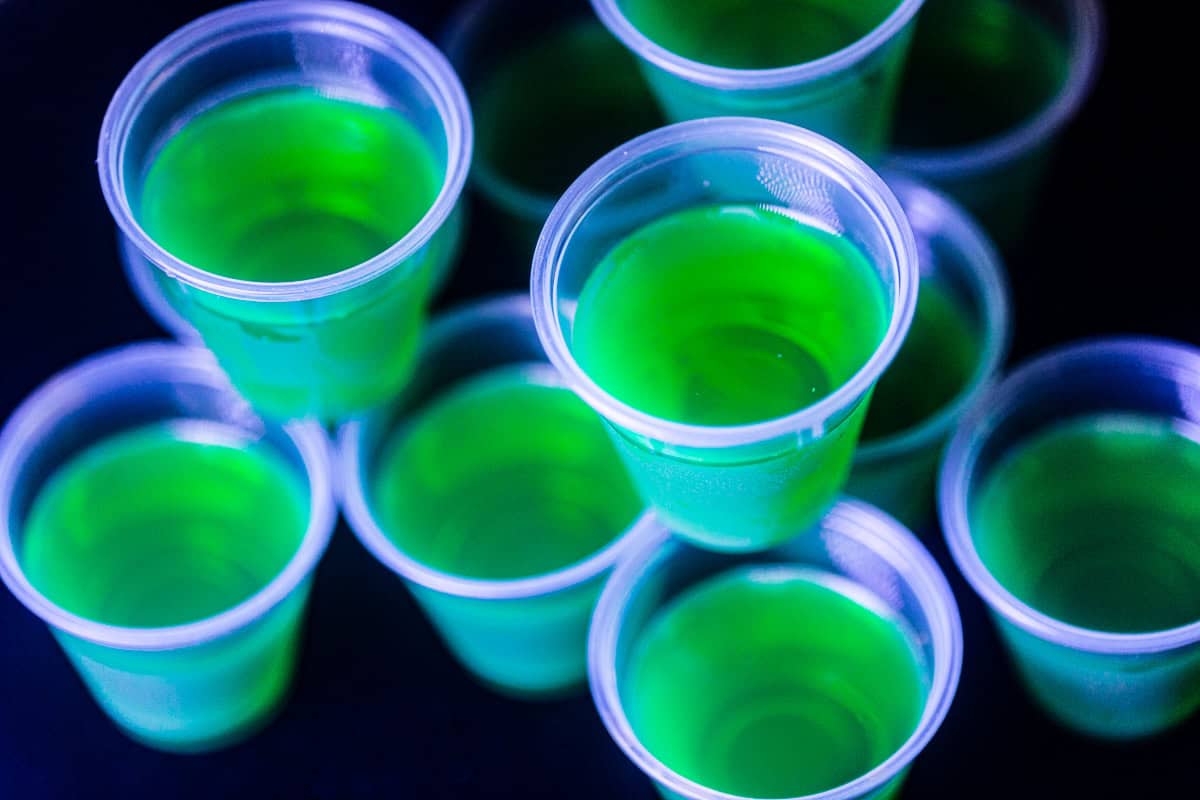 Overhead view of green colored glow in the dark jello shots under a black light.