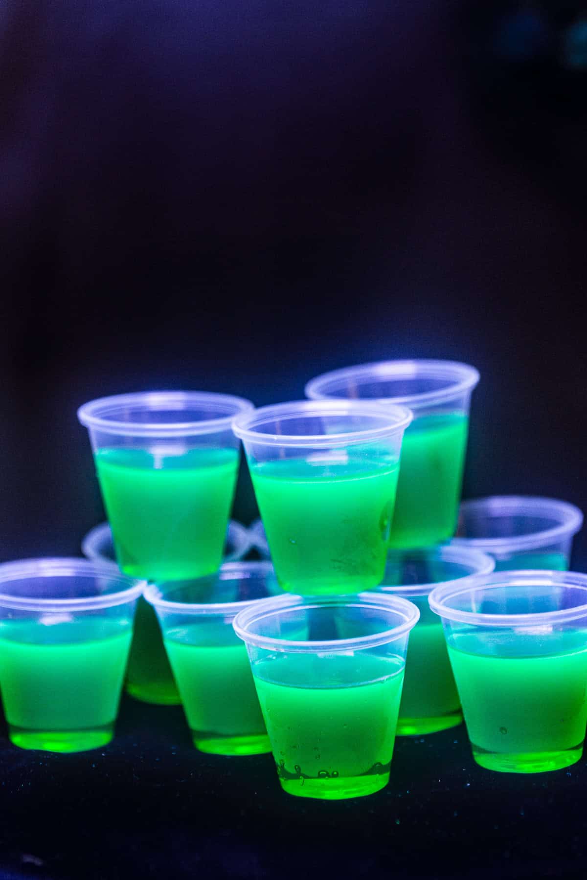 Green glowing vodka tonic jello shots shown under a blacklight.