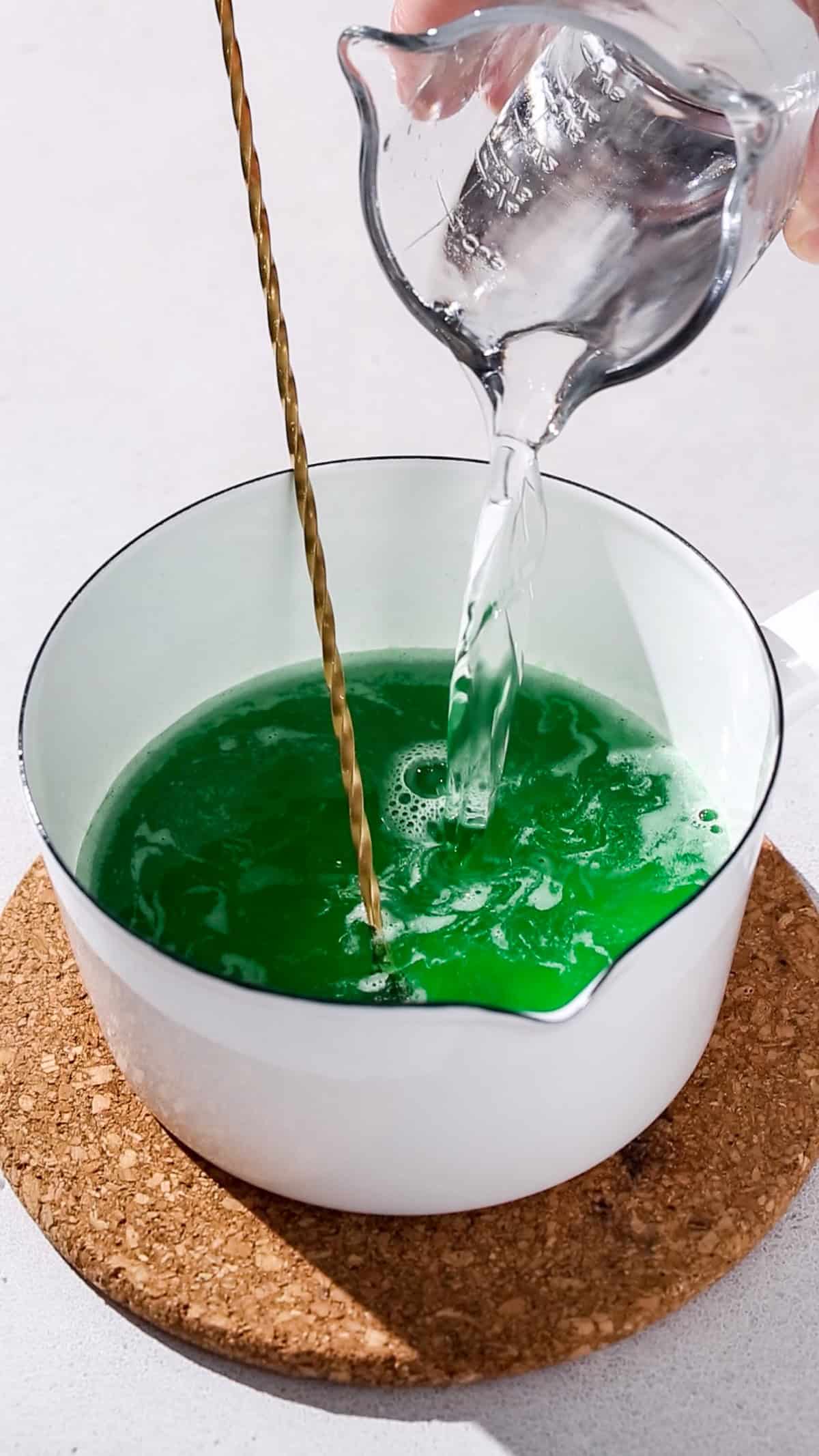 Hand adding vodka to the cooled tonic and jello mixture.