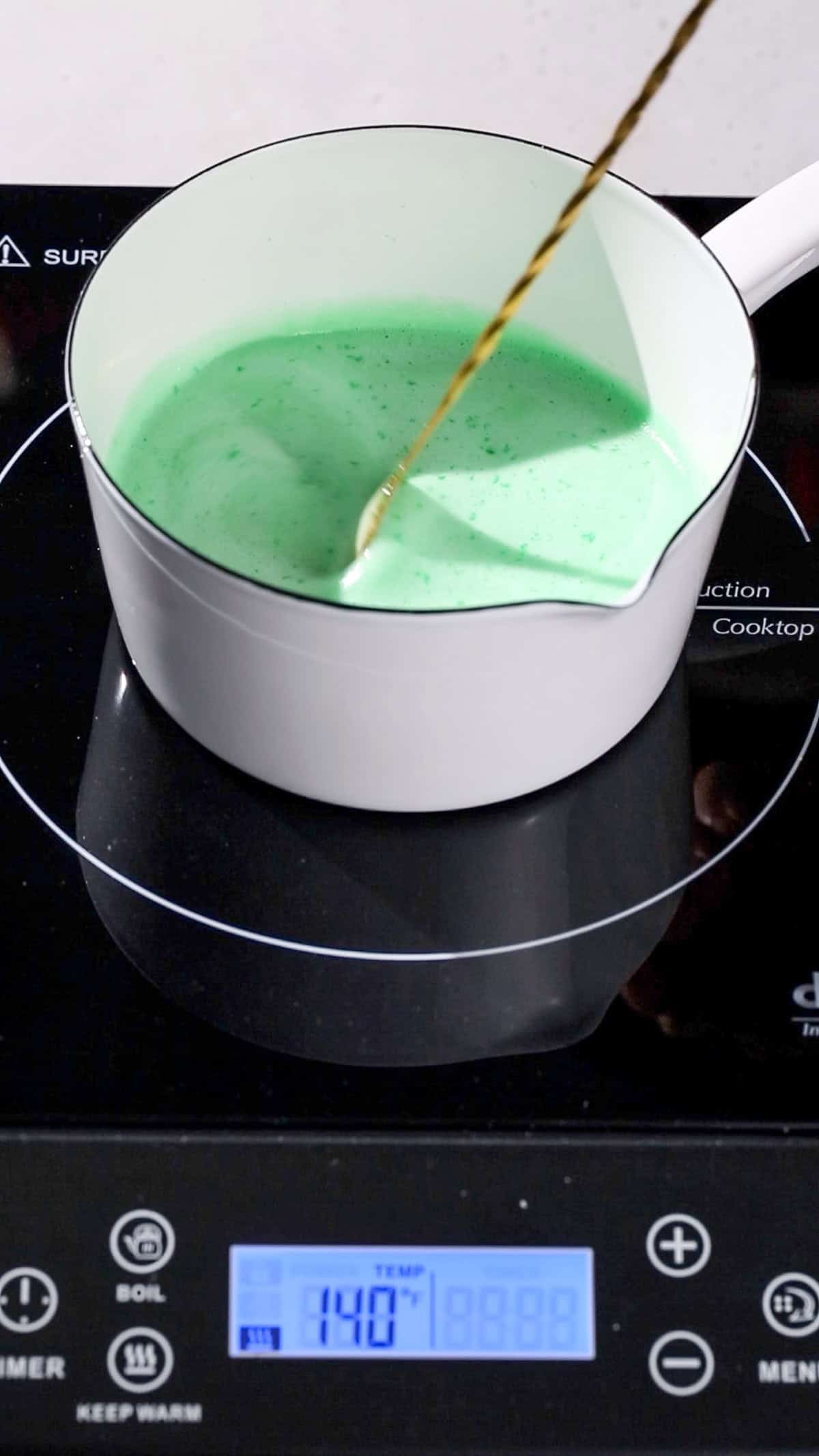 Hand using a bar spoon to stir the jello and tonic mixture while it heats.