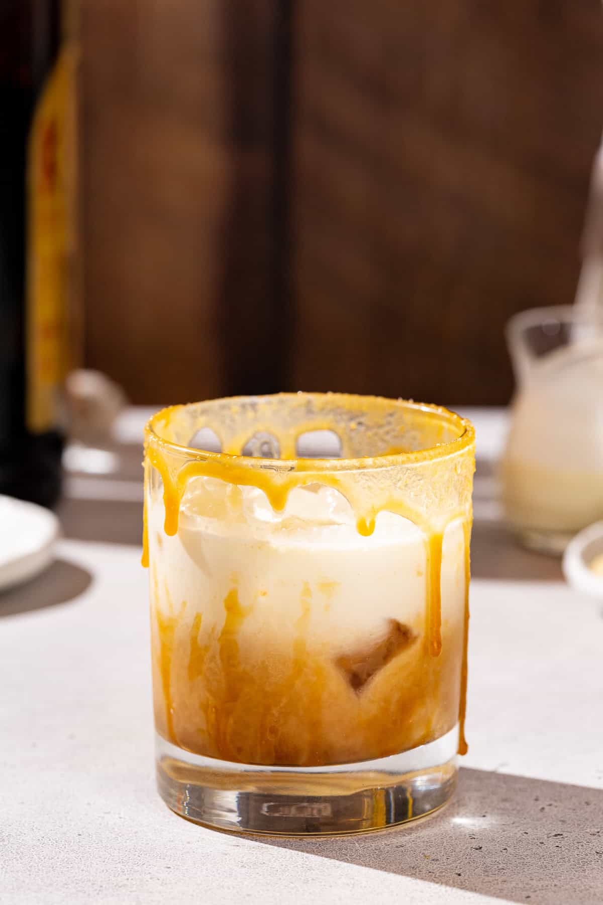 Side view of a creamy Maple caramel white Russian cocktail. The drink is dripping with caramel drizzle and served over ice in an old fashioned glass.