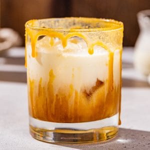 Close up of a White Russian caramel maple cocktail on a countertop. A caramel maple sugar drizzle is on the rim and side of the glass.