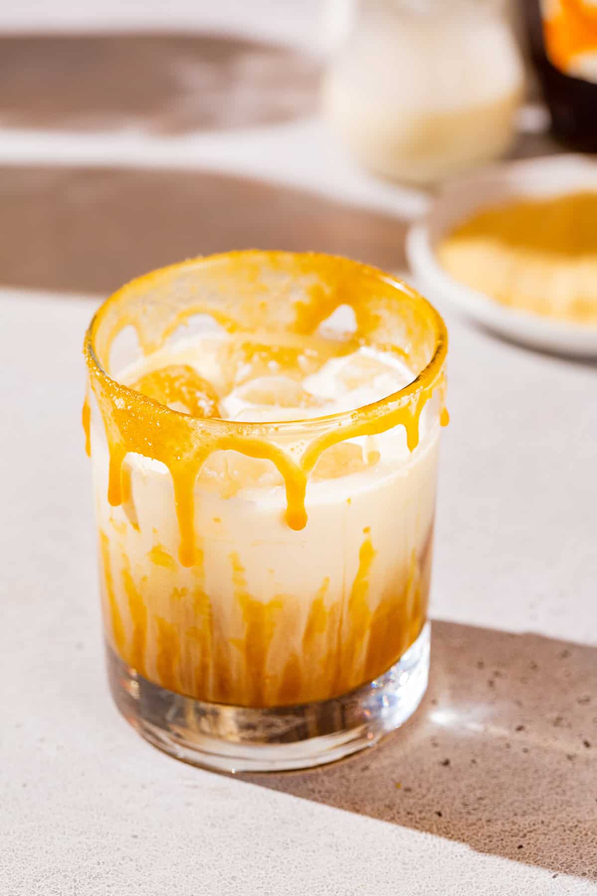 Maple Caramel White Russian cocktail on a countertop with maple sugar and cream in the background.