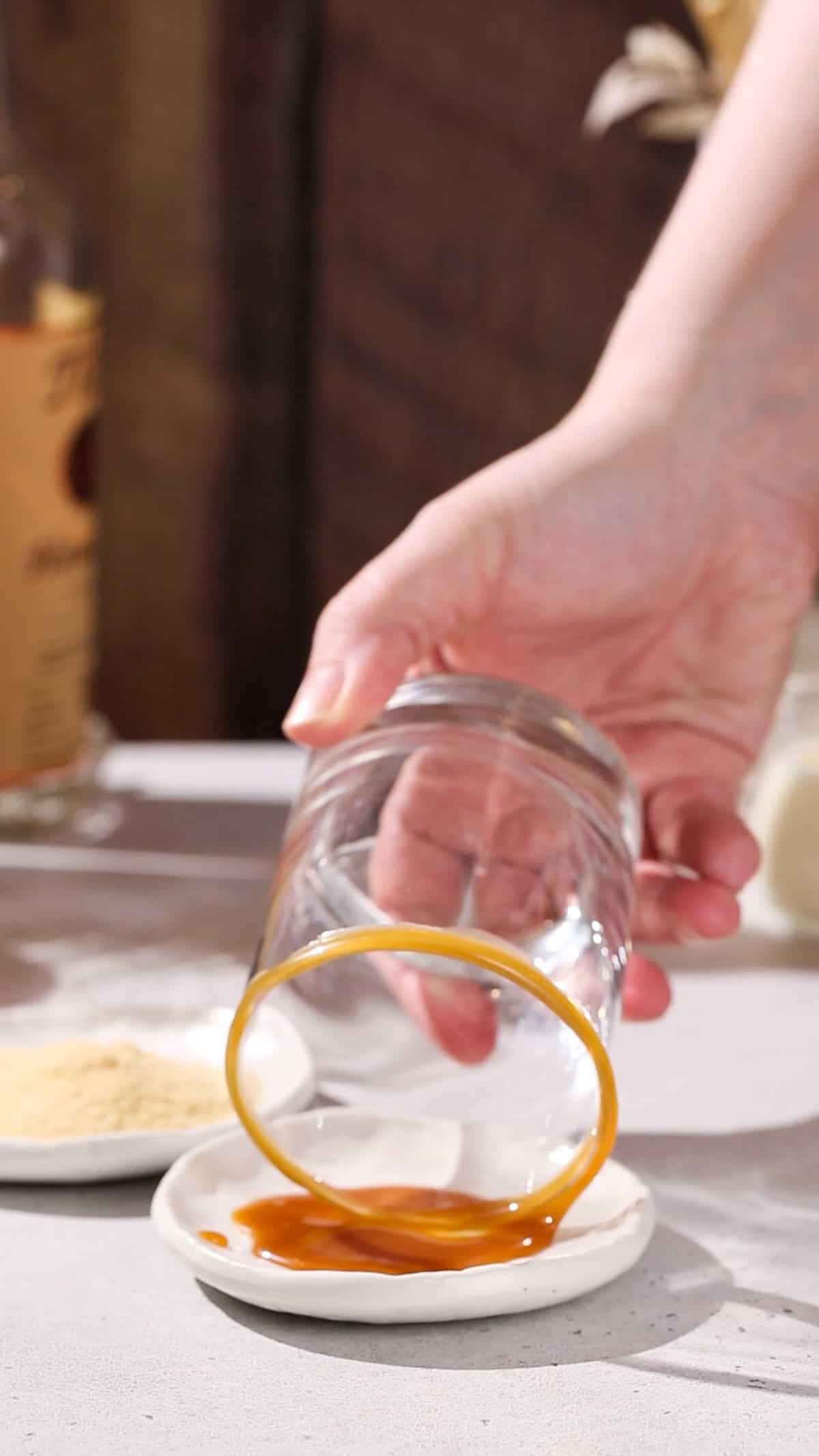 Hand dipping the rim of a cocktail glass into a dish of caramel sauce.