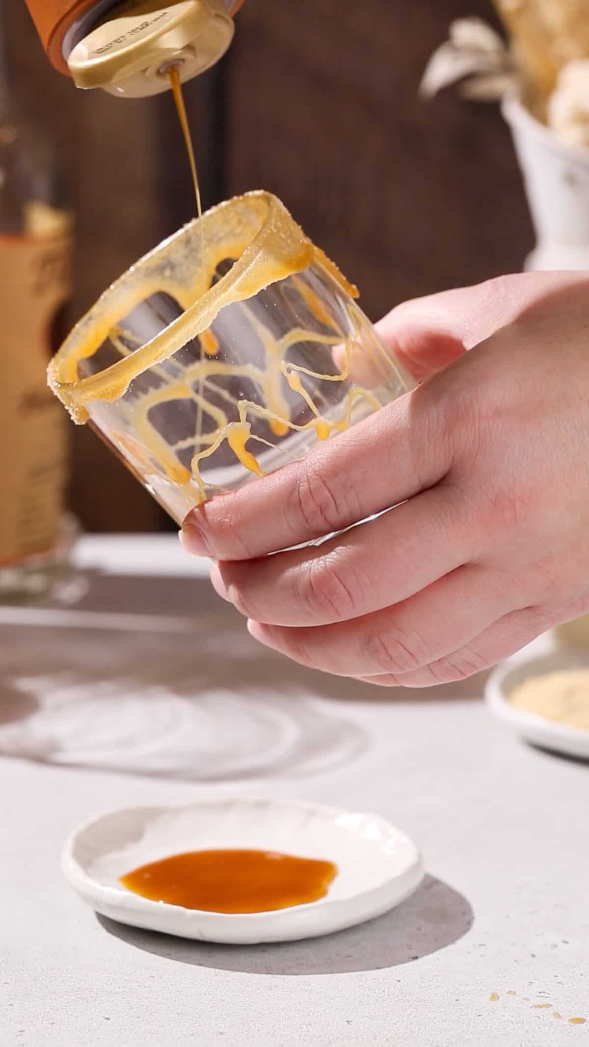 Hand dripping caramel sauce into a cocktail glass.