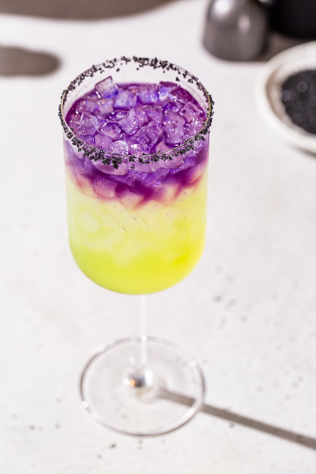 Overhead view of a Witches’ Brew cocktail with a green layer on the bottom and purple layer on top and a black salt rim.