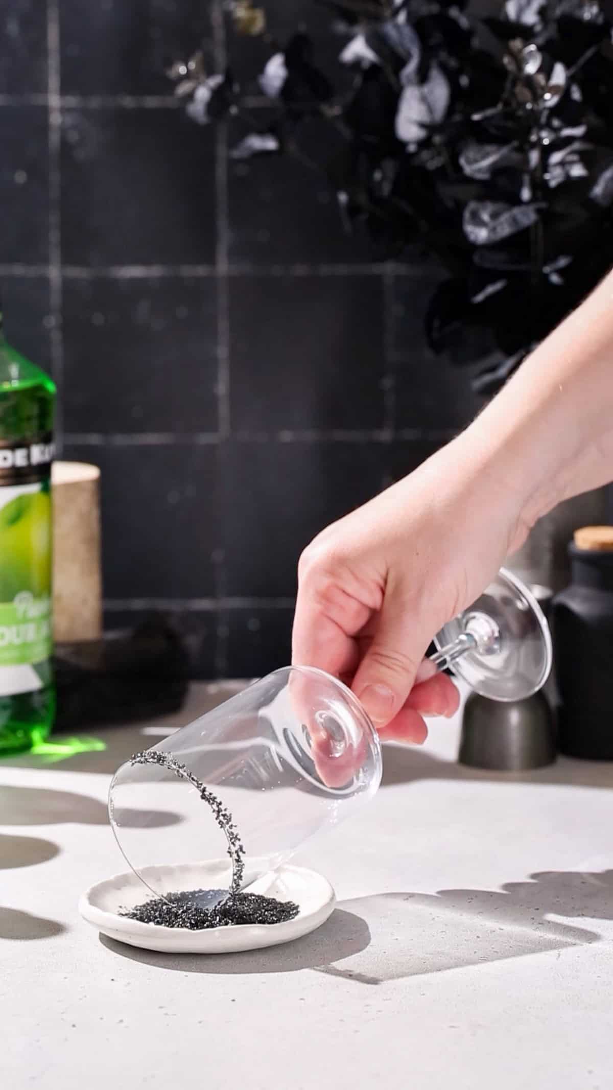 Hand dipping the rim of a cocktail glass into a dish of black salt.