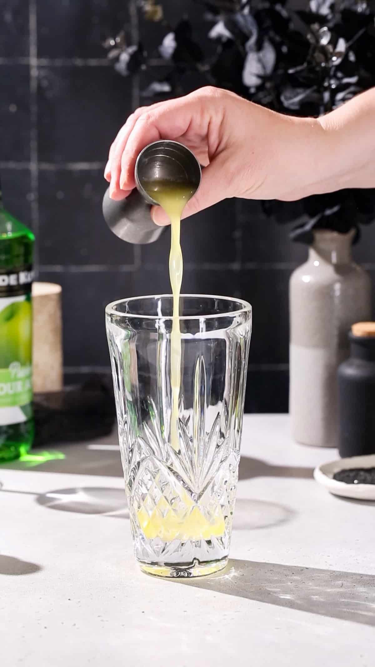 Hand adding pineapple juice to a cocktail shaker.