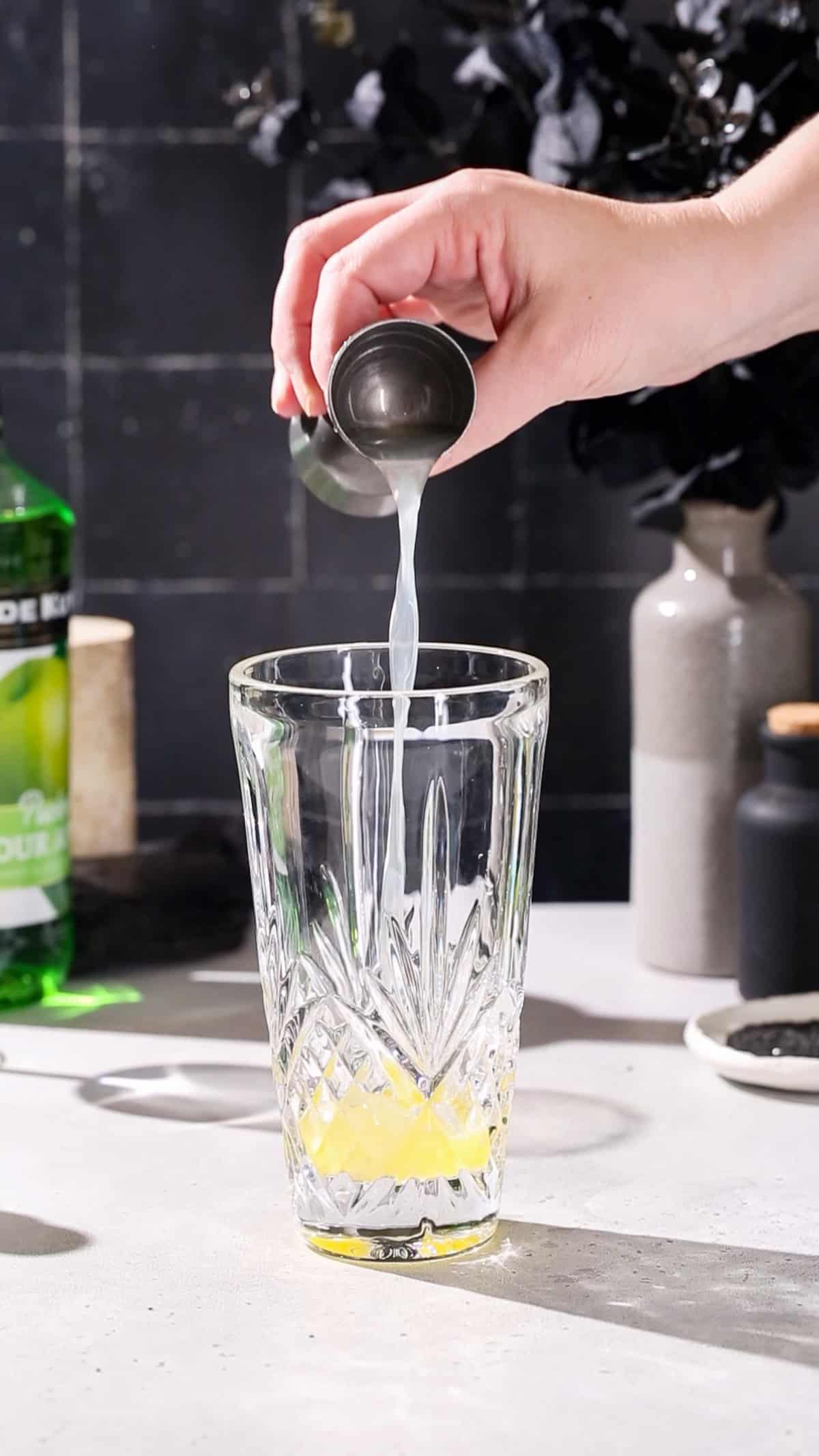 Hand adding lime juice to a cocktail shaker.