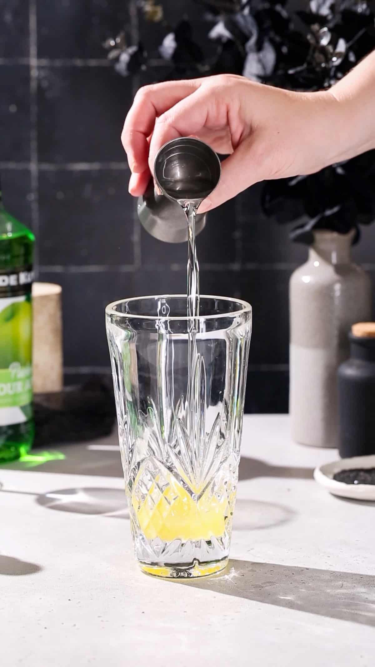 Hand adding simple syrup to a cocktail shaker.