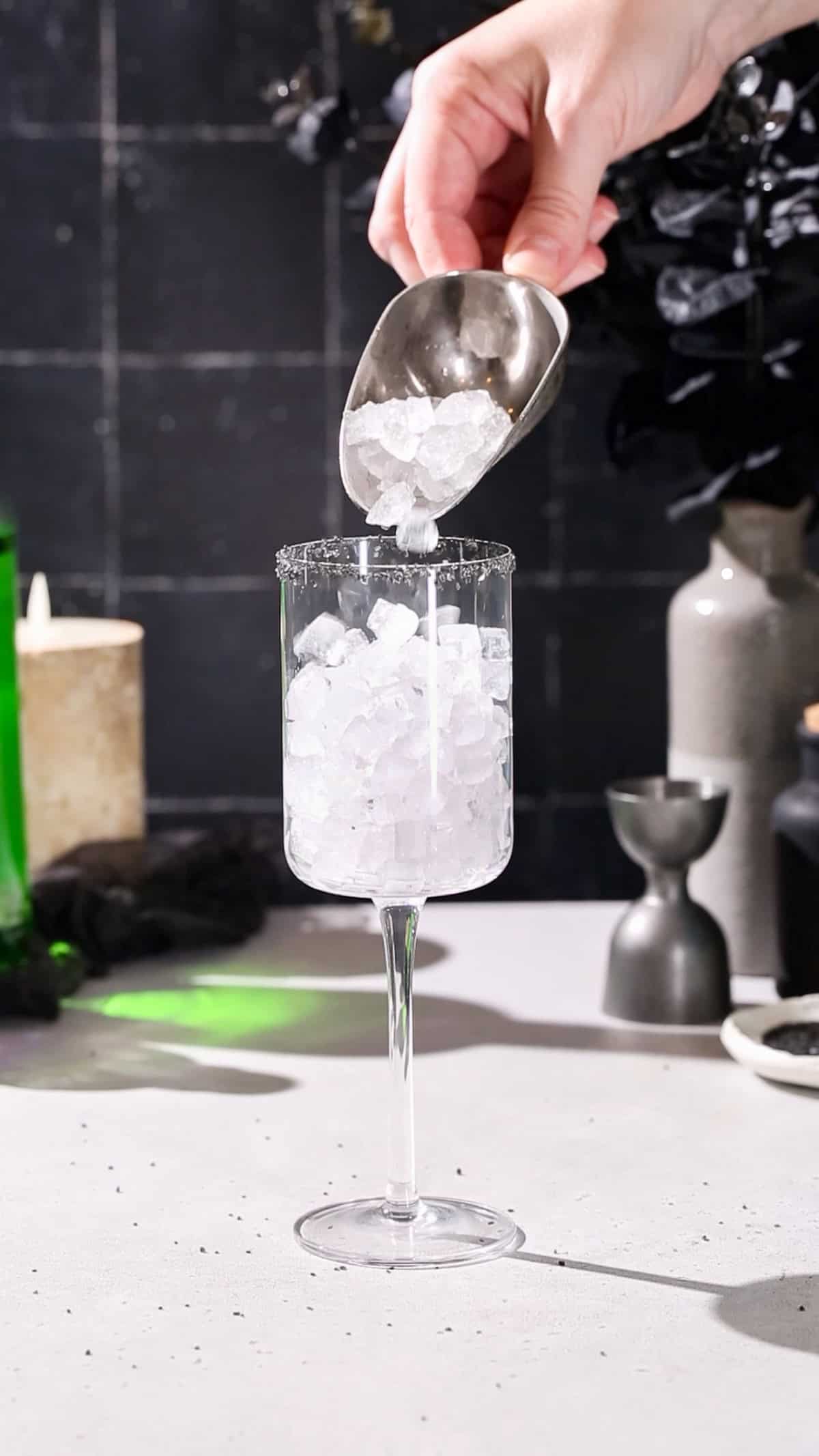 Hand adding pebble ice to a tall wine glass using an ice scoop.