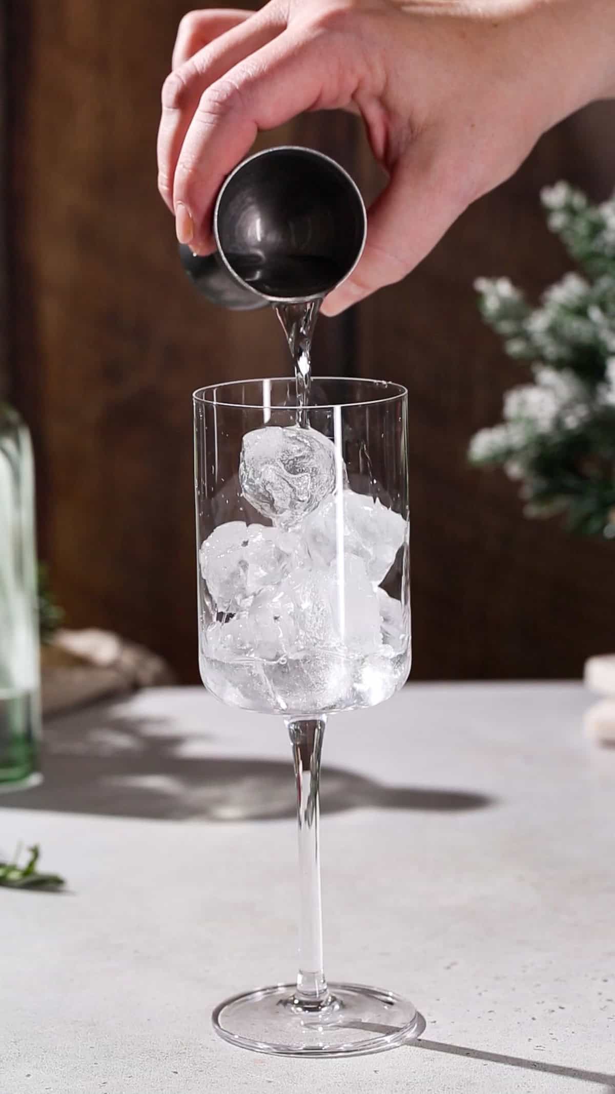 Hand adding gin to a cocktail glass filled with ice.