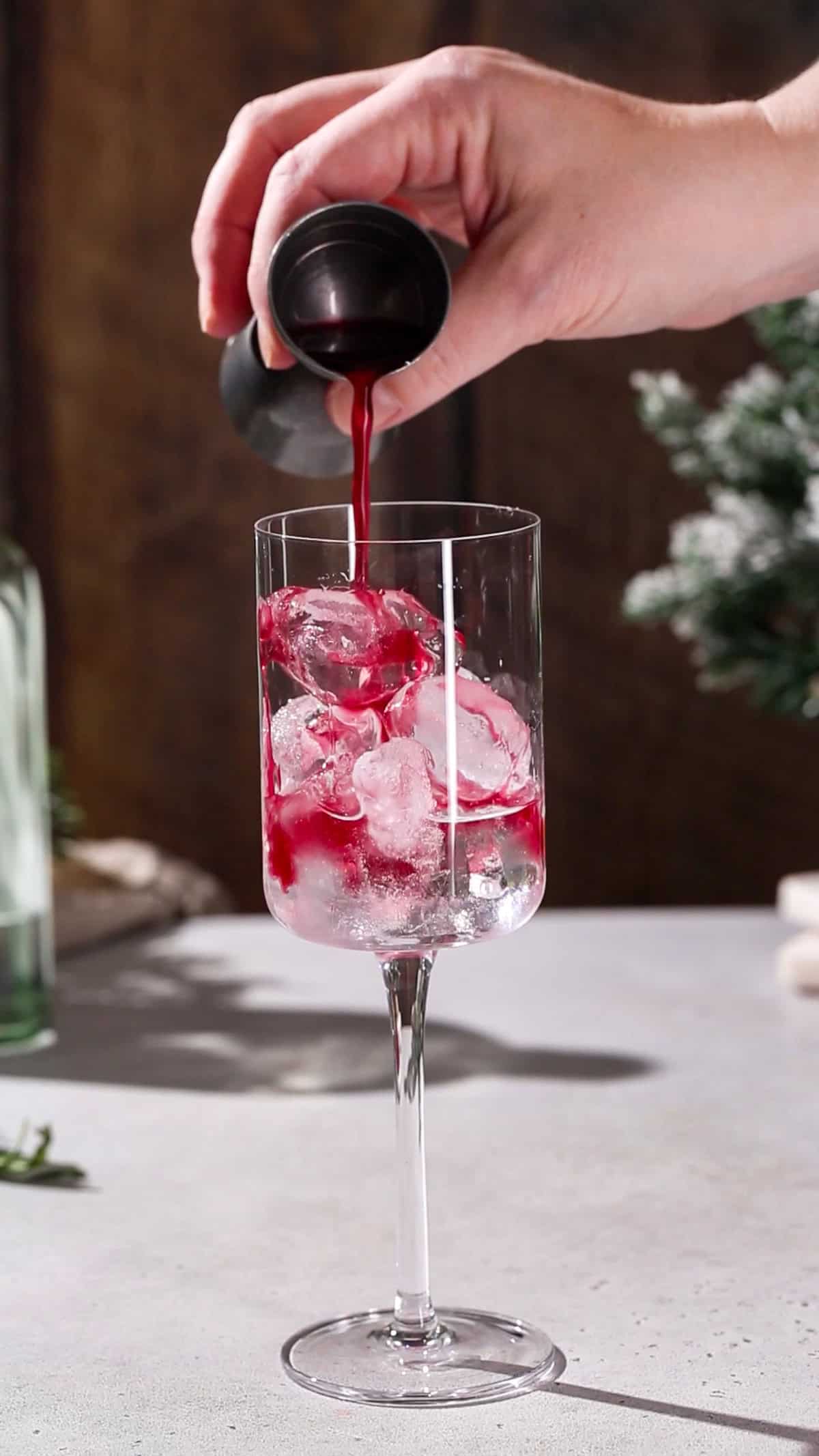 Hand adding pomegranate juice to a cocktail glass.