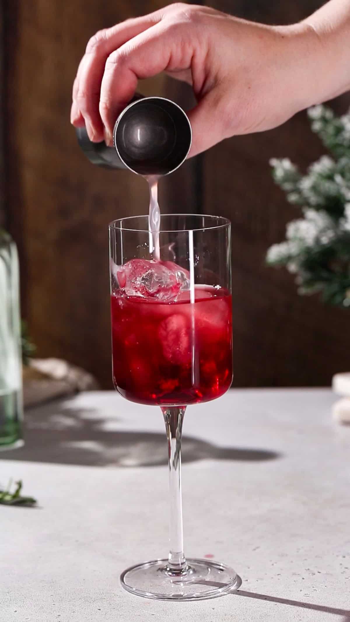 Hand pouring lime juice into a cocktail glass filled with red liquid.