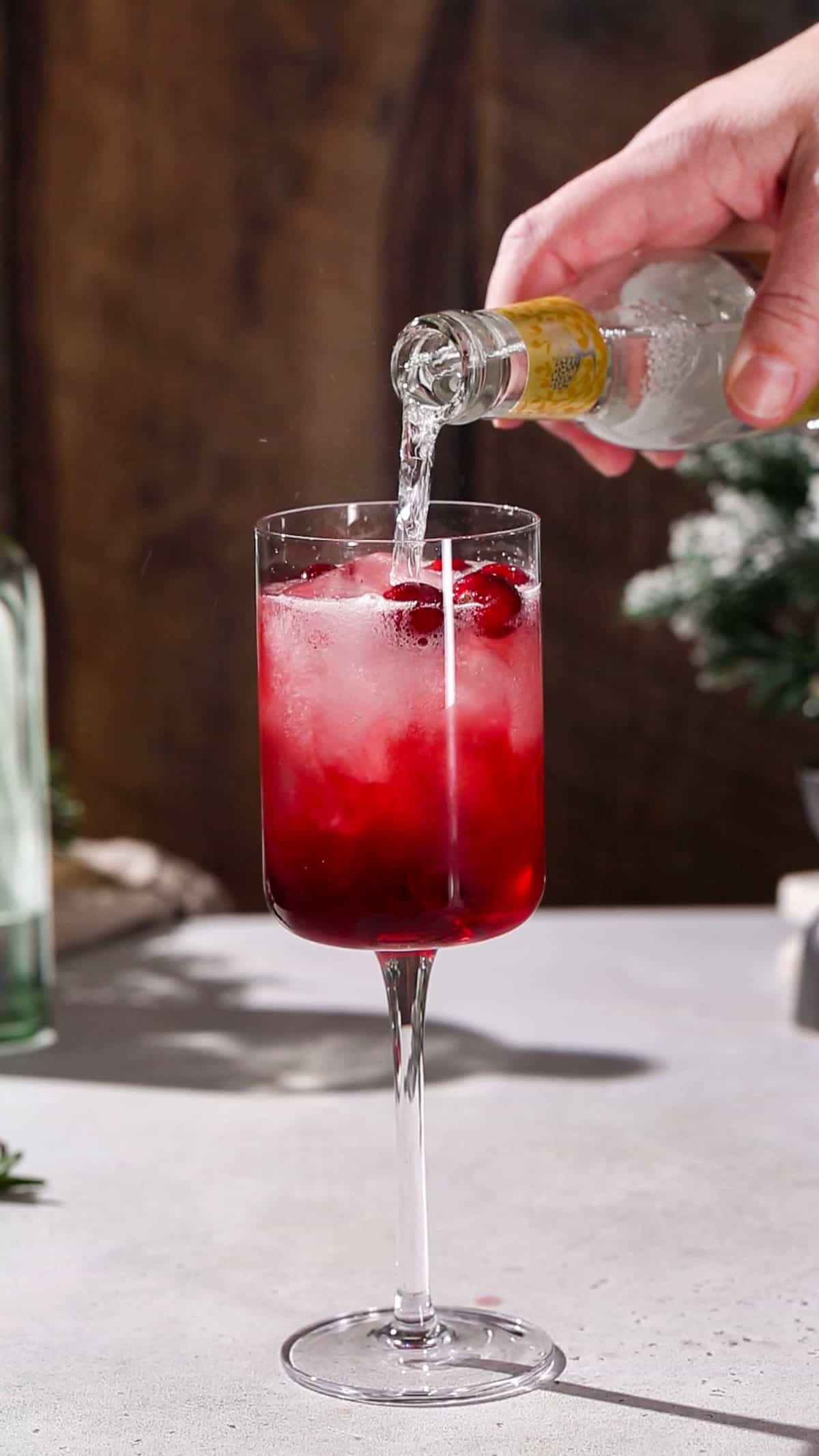 Hand adding tonic water to a red cocktail.