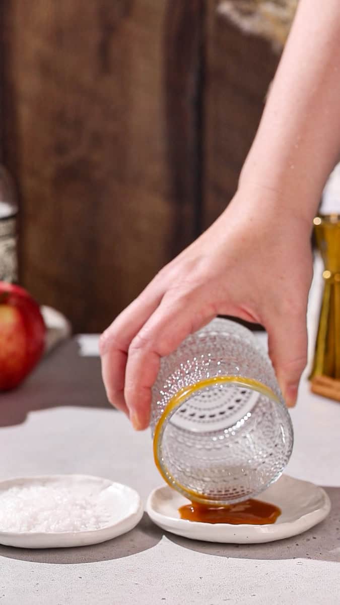 Hand dipping cocktail glass into a dish of caramel.