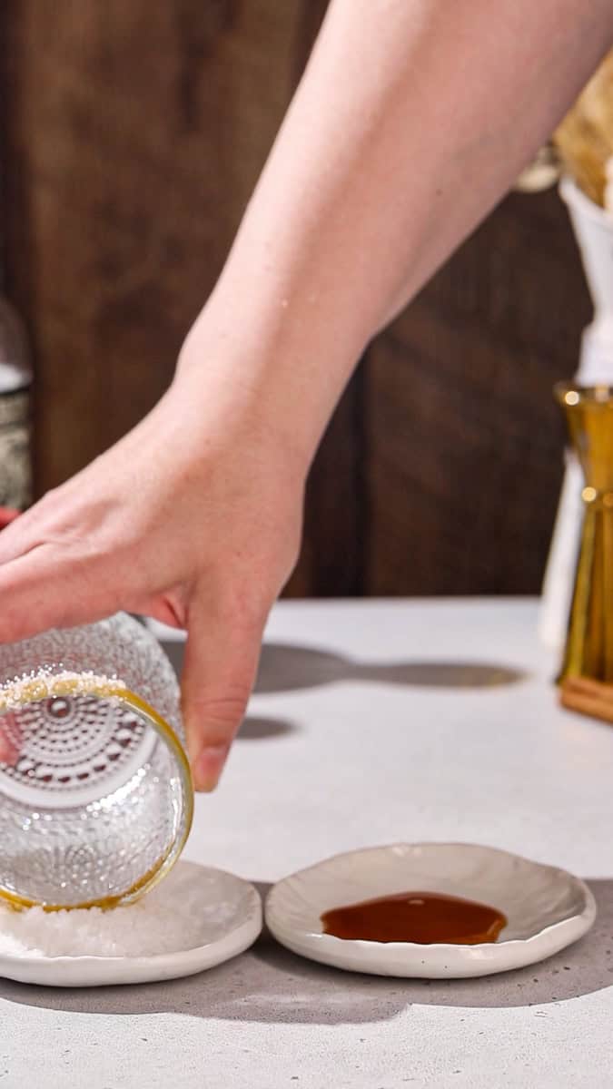 Hand dipping cocktail glass into a dish of salt.