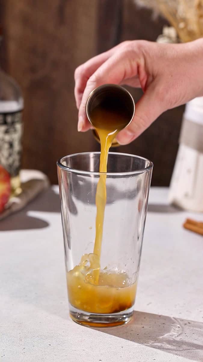 Hand pouring apple cider into a cocktail shaker.