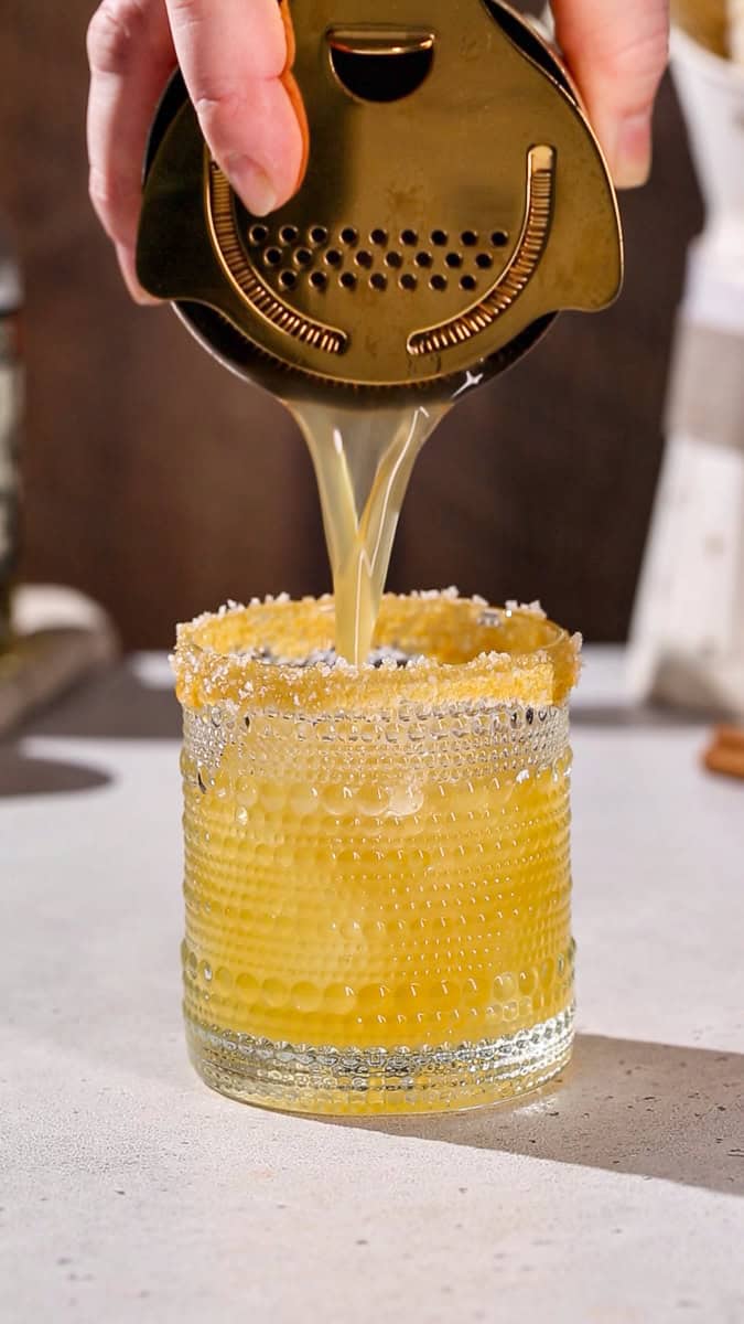 Hand straining a cocktail in a cocktail glass with a salted caramel rim.