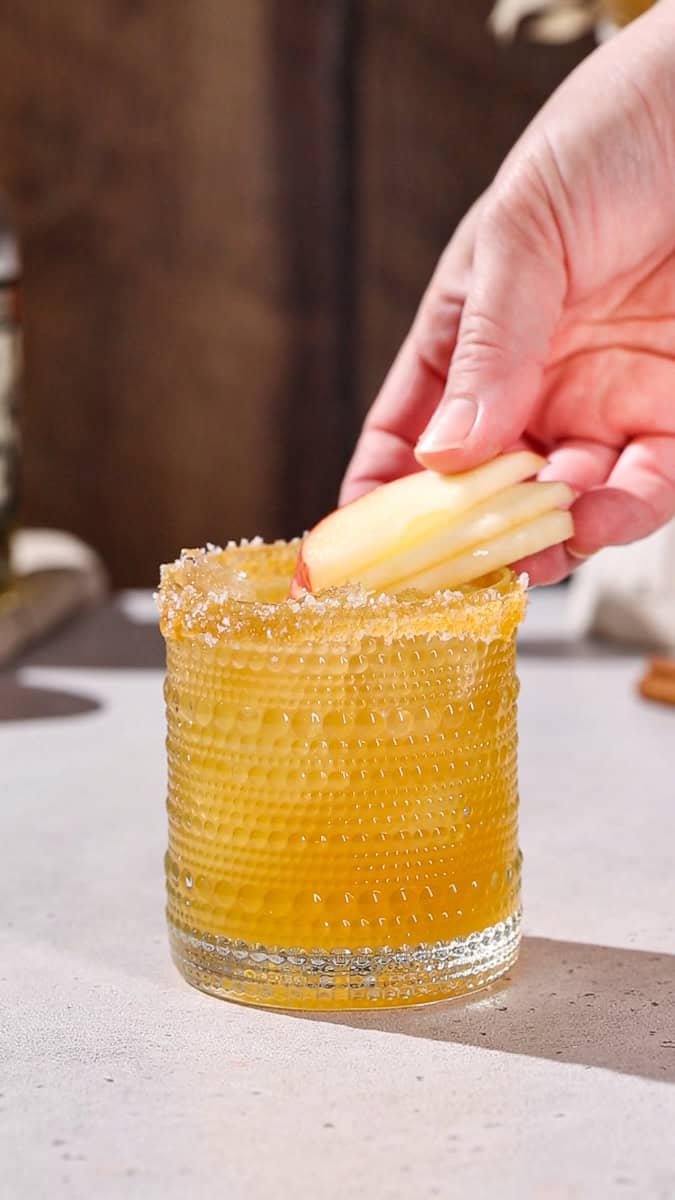 Hand adding apple slices to garnish a cocktail.