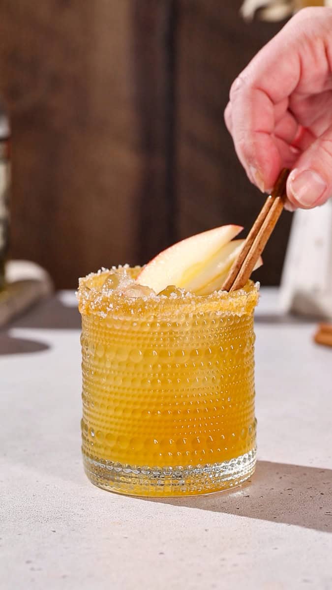 Hand adding a cinnamon stick to garnish a cocktail.