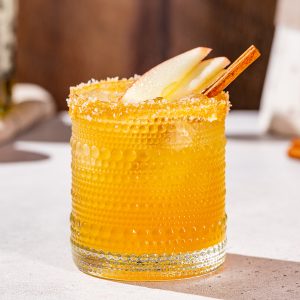 Thanksgiving Margarita on a countertop with apple slices and cinnamon stick garnish.