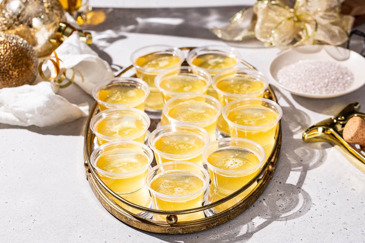 Slightly overhead view of Champagne Jello Shots on a mirrored tray with gold decor in the background.