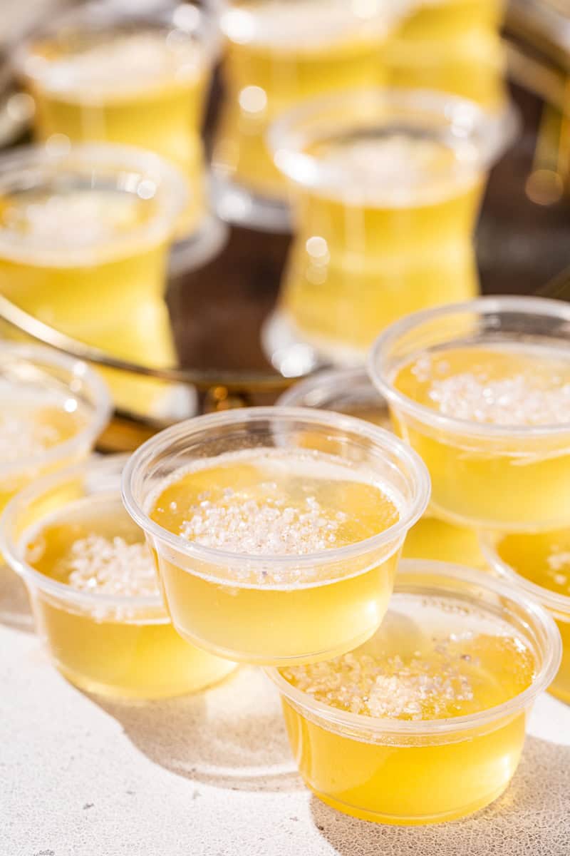 Close up of plastic cups filled with Champagne jello shots. On the top is some silver sanding sugar as a garnish.