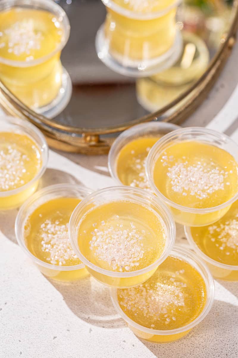 Champagne jello shots on a countertop with some of them on a gold mirrored tray in the background.