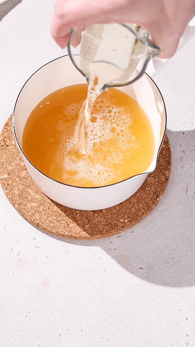 Hand adding Champagne into a saucepan.