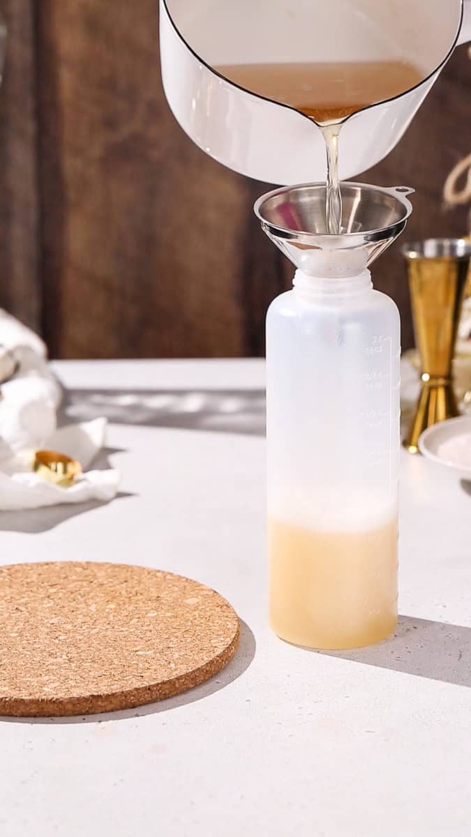 Hand using a funnel to add the gelatin mixture to a squeeze bottle.