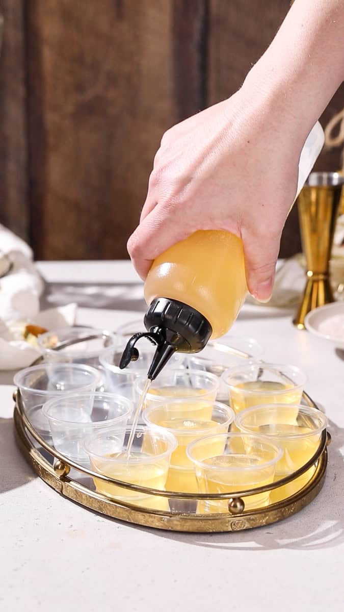 Hand using a squeeze bottle to add gelatin mixture to mini cups.